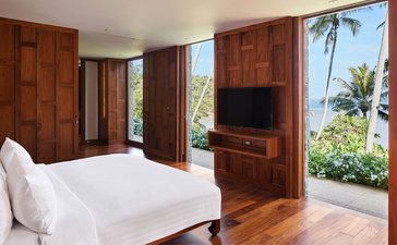アマンプリのナインベッドルームオーシャンヴィラの主寝室。木製キャビネット、白いベッド、大きな窓から海とヤシの木が見える。