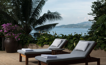 Two lounge chairs on a sandy terrace at Amanpuri resort, overlooking tropical waters and distant mountains.