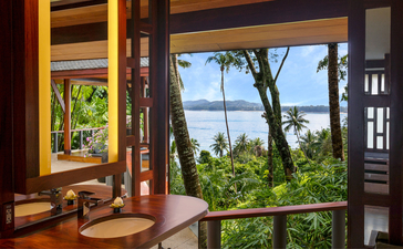 Pavilion interior at Amanpuri resort with open doors framing views of tropical palms and coastline.