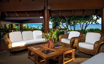 Wooden lounge furniture with cream cushions and potted plants on a covered terrace at Amanpulo, Philippines.