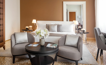 安缦威尼斯酒店的帕拉佐宫殿明亮套房,配有米色墙壁、灰色扶手椅和柔和照明。