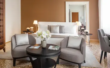 Palazzo Chamber Luminoso at Aman Venice hotel: serene principal bedroom with grey seating area, neutral tones, and Venetian views.