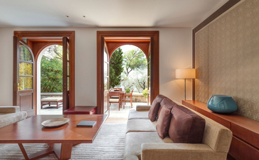 Queen Marija Suite at Aman Sveti Stefan with French doors opening to Adriatic views, neutral furnishings and wooden accents.