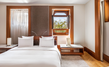 Principal bedroom at Aman Sveti Stefan with twin beds, wooden furnishings, and coastal views through framed window.