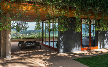 Sala con vista sull'oceano presso la villa Amanpuri in Tailandia, con arredamenti in legno naturale e aperture verso la terrazza esterna.