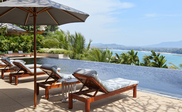 Sunbeds and parasol on a sandy beach terrace overlooking the sea at Amanpuri resort, Thailand.