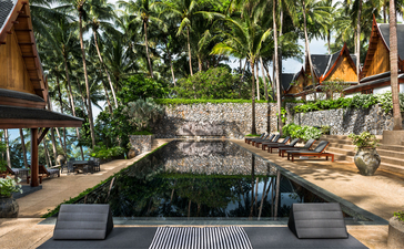 Reflective water channel lined with tropical plants at Amanpuri resort, Thailand.