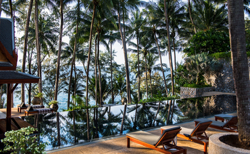 Amanpuri resort courtyard with palm trees, lounge seating and ocean view beyond.