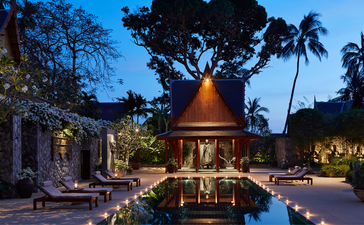 Twilight view of a Thai-style pavilion beside an illuminated pool at Amanpuri resort, Thailand, with palm trees and evening lighting.