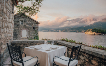 St. Sava Cottage dining area at Aman Sveti Stefan with Adriatic Sea views at dusk.