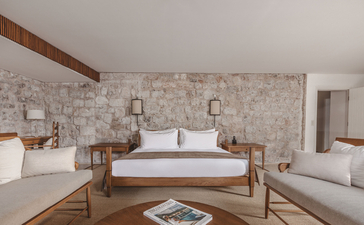 Principal bedroom at St. Sava Cottage, Aman Sveti Stefan, with stone walls and wooden bed frame.