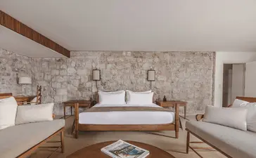 Principal bedroom at St. Sava Cottage, Aman Sveti Stefan, with stone walls and wooden bed frame.