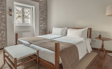 St. Sava Cottage principal bedroom at Aman Sveti Stefan, with wooden bed frame and neutral bedding.