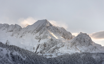 Snow-covered alpine peaks above forested slopes at Aman Le Mélézin, French Alps.