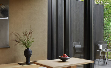 Susuki Room at Aman Kyoto, with wooden platform seating, ikebana arrangement, and garden views through glass doors.