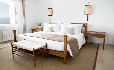 Principal bedroom in the Sveti Stefan Suite at Aman Sveti Stefan, with wooden bed frame and neutral furnishings overlooking the Adriatic coast.