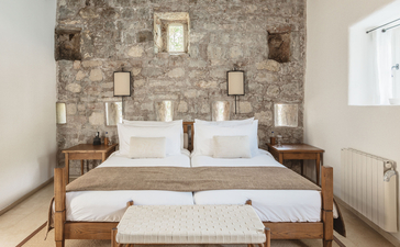 Three-bedroom village cottage at Aman Sveti Stefan with principal bedroom featuring stone feature wall and wooden bed frame.