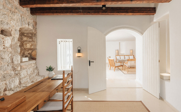 Three-bedroom village cottage interior at Aman Sveti Stefan, Montenegro, with arched doorway and wooden beams.