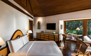 アマンプロのリゾートにある2ベッドルームヴィラの寝室。木製の天井、白い壁、大きなベッド、テレビ、窓からの緑の眺め。