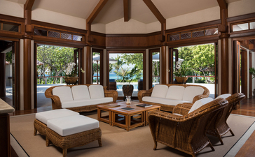 アマンプロのツーベッドルームヴィラの居間。木製の梁天井と大きな窓から庭園が見える。