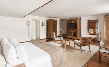 Two-bedroom suite at Aman Sveti Stefan with bed, seating area, and wooden furnishings throughout.