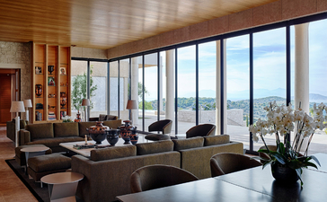 Principal bedroom suite at Amanzoe resort overlooking the Aegean coast through floor-to-ceiling windows.