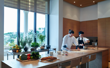 Réception d'Amanzoe avec personnel accueillant les visiteurs, baies vitrées donnant sur la côte grecque.