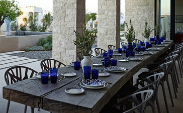 Outdoor dining table set with blue chairs and place settings at Amanzoe resort, Greece.
