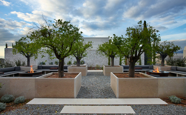 Courtyard at Amanzoe resort with symmetrical pathways, potted trees, and Aegean Sea views beyond.