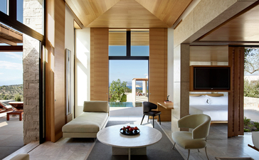 Villa living area at Amanzoe resort, with cream walls, round table, and views across the Aegean landscape.