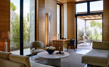 Villa 20 sitting area with floor-to-ceiling windows overlooking Amanzoe resort grounds, Greece.