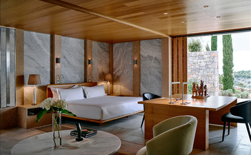 Principal bedroom at Amanzoe resort with wooden panelling, floor-to-ceiling windows and views across the Greek landscape.