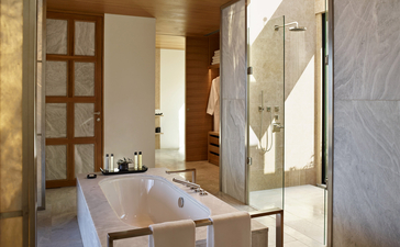 Villa bathroom at Amanzoe resort with marble surfaces and wooden door.