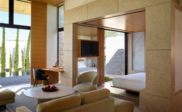 Principal bedroom with en-suite bathroom at Amanzoe resort, Greece, featuring warm travertine finishes and natural light.