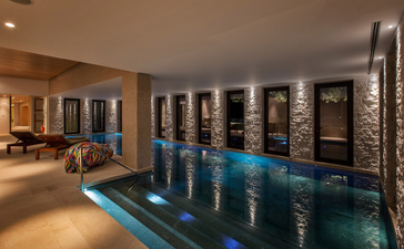 Spa pool at Amanzoe resort, flanked by dark wooden doors and warm ambient lighting.
