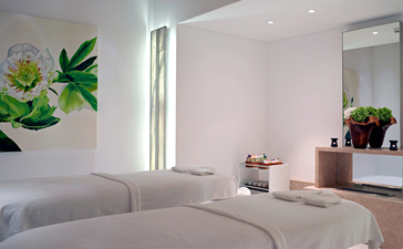 Principal bedroom at Amanzoe resort with curved bed, soft natural light, and potted plants.