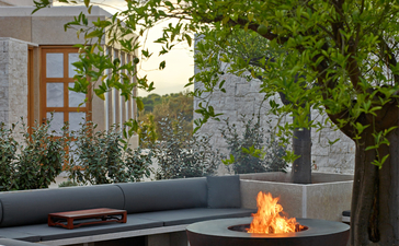 Outdoor seating area at Amanzoe resort with a modern fireplace and verdant climbing plants against stone walls.