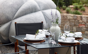 Outdoor dining setup at Amanzoe resort with a draped grey canopy, set table, and Mediterranean views.
