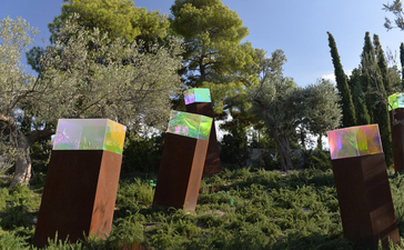 Colourful metal sculptures nestled among cypress trees and lush vegetation at Amanzoe resort, Greece.