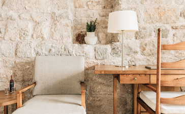 Principal bedroom at Aman Sveti Stefan with stone walls, wooden desk and cream bedding.