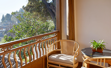 Wooden balcony at Amandayan with carved railings, comfortable seating, and mountain views through open doors.