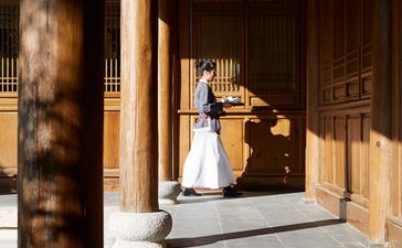 Woman in traditional dress standing beneath wooden columns at Amandayan.