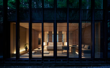 Pavilion bedroom at Aman Kyoto lit warmly at dusk, with floor-to-ceiling glass doors opening onto a dark courtyard.