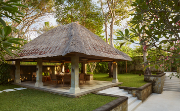 Thatched-roof dining bale at Aman Villas at Nusa Dua, surrounded by manicured gardens and tropical vegetation.