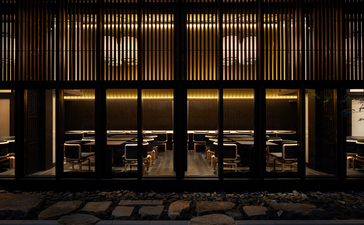 Aman Kyoto's dining venue entrance with wooden latticed doors illuminated by warm lighting at dusk.