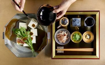 Overhead view of a Japanese dining table at Aman Kyoto with ceramic dishes, fresh vegetables, and traditional wooden serving trays.