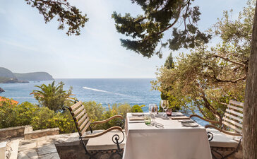 Dining piazza at Aman Sveti Stefan with sea views, wooden loungers and table setting overlooking the Adriatic coast.