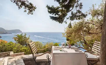 Dining piazza at Aman Sveti Stefan with sea views, wooden loungers and table setting overlooking the Adriatic coast.