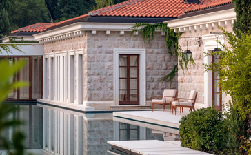Waterfront pavilion at Aman Sveti Stefan with classical columns and terracotta roof reflected in still water.