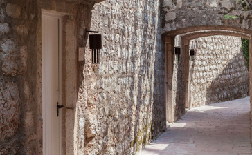 Stone corridor with weathered arches at Aman Sveti Stefan, morning light casting shadows on aged walls.